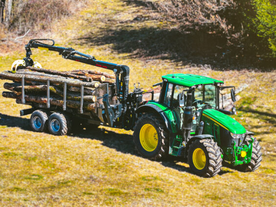 Grønn John Deere traktor med en fullastet PALMS 8D tømmervogn i solfylt terreng.