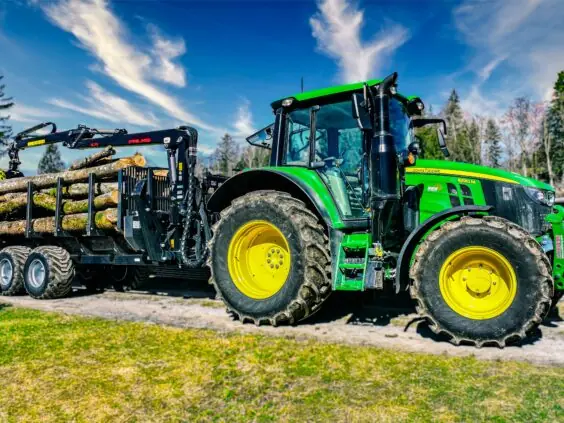 John Deere traktor med tømmertilhenger og en PALMS 4.71 skogskran lastet med tømmerstokker.