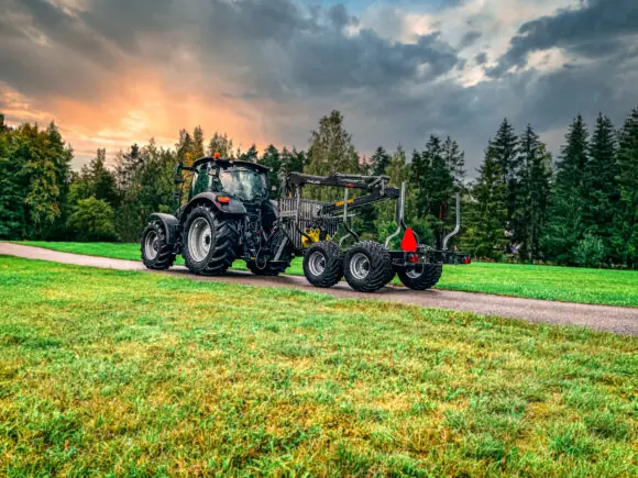 Svart traktor med en PALMS 2.54 skogskran på en tømmervogn langs en vei.