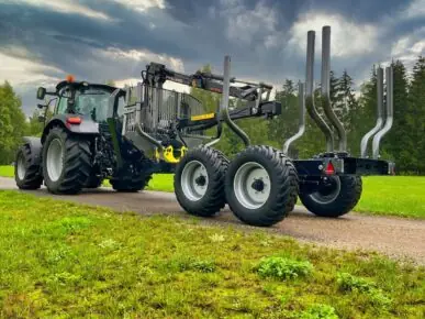 En traktor med en PALMS 10D tømmervogn på en grusvei i landlige omgivelser.