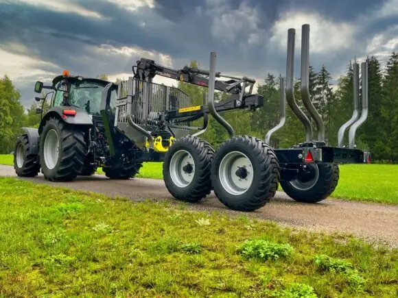 En traktor med en PALMS 10D tømmervogn på en grusvei i landlige omgivelser.