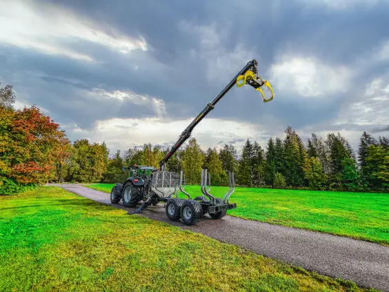 Traktor med PALMS 5.75 skogskran montert på tømmervogn på en vei i grønne omgivelser.