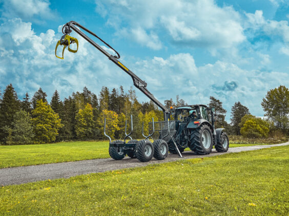 Traktor med PALMS 3.63 skogskran montert på tømmerhenger langs en grønn mark.