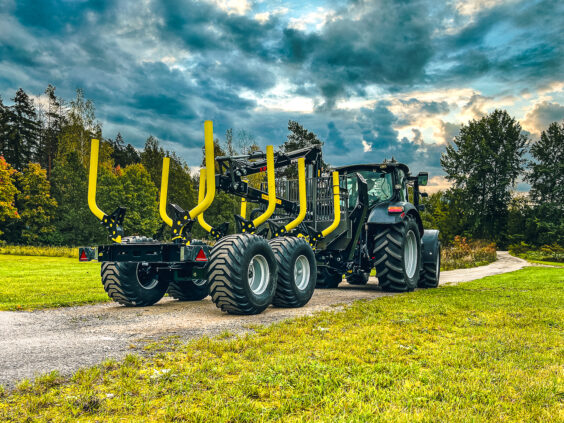 En traktor med en PALMS 8D tømmervogn på en grusvei i grønne omgivelser.