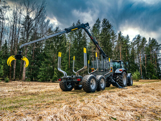 En PALMS 12D tømmervogn trukket av en traktor i et skogsområde.