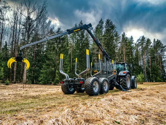 En PALMS 12D tømmervogn trukket av en traktor i et skogsområde.