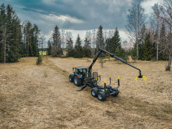 En traktor med en PALMS 12D tømmervogn på et åpent gressfelt under en skyet himmel.