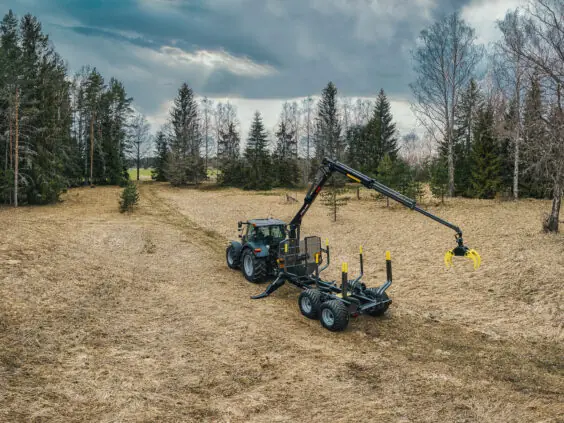 En traktor med en PALMS 12D tømmervogn på et åpent gressfelt under en skyet himmel.