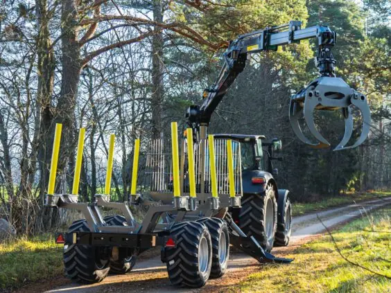 En traktor med tømmervogn og PALMS 5.85 skogskran på en skogsvei i solskinn.