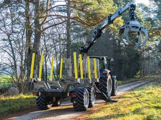 En traktor med tømmervogn og PALMS 5.85 skogskran på en skogsvei i solskinn.