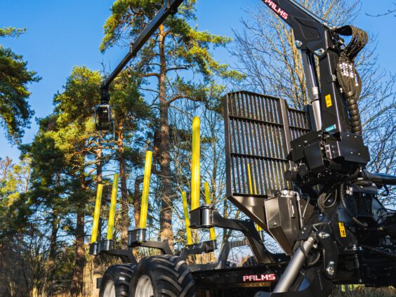 En svart PALMS 5.85 skogskran montert på en tømmervogn i solfylt skogsterreng.