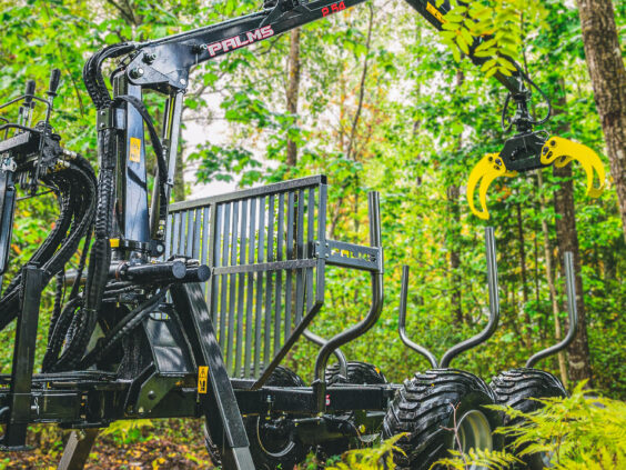 Robust PALMS 6S tømmervogn med kran stående i grønne skogsomgivelser.