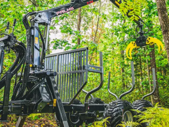 Robust PALMS 6S tømmervogn med kran stående i grønne skogsomgivelser.