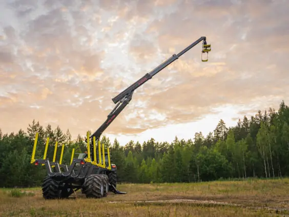 Kraftig PALMS X100 skogskran utstrakt på en tømmervogn foran skog og solnedgang.