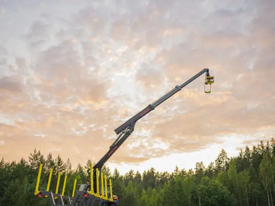 En PALMS X100 skogskran montert på en tømmervogn, utstrakt mot en vakker solnedgang.