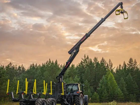 Traktor med tømmerhenger og en fullt utstrakt PALMS X100 skogskran mot en vakker solnedgang.