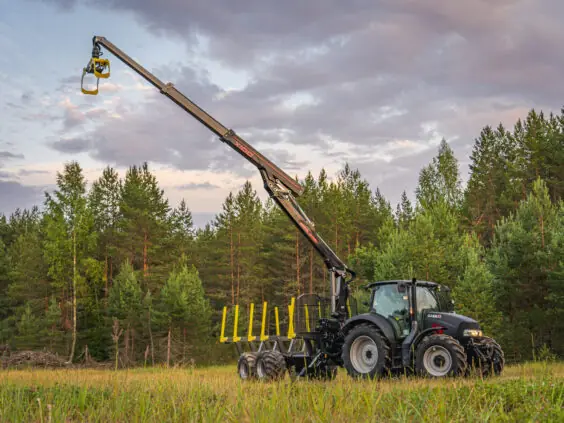 Svart traktor med en fullt utstrakt PALMS X100 skogskran og tømmertilhenger på et jorde.