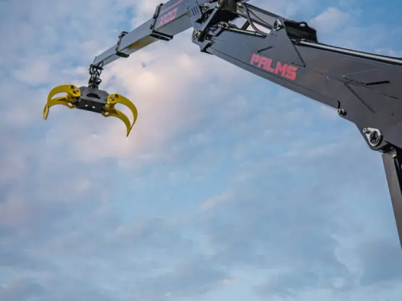 PALMS X100 skogskran med gul tømmerklo hevet mot en blå og skyete himmel.