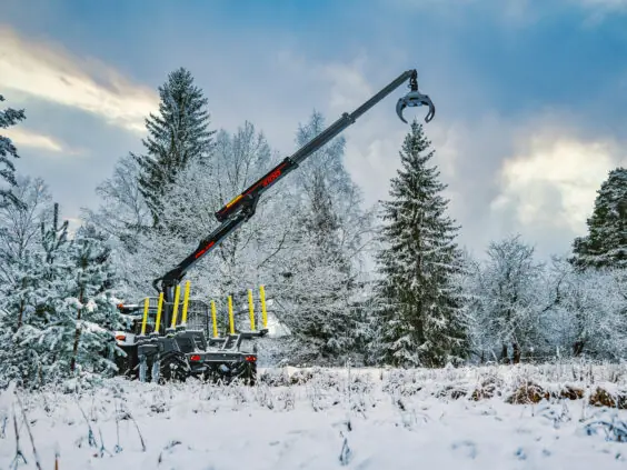 En kraftfull PALMS HMWD 3.2 tømmervogn i et snødekket vinterlandskap med kranen hevet.