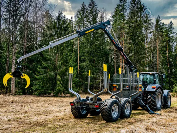 En PALMS 12D tømmervogn trukket av en traktor i et skogsområde.
