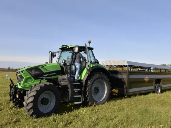 En grønn Deutz-Fahr traktor som trekker en PT4800-HS dyrehenger på et jorde.