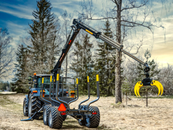 En PALMS 12D tømmervogn trukket av en traktor i et skogsområde.