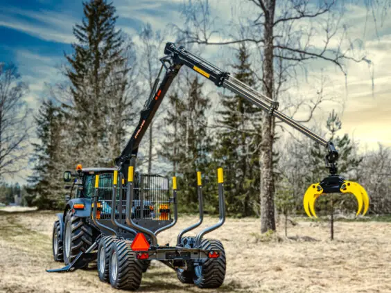 En PALMS 12D tømmervogn trukket av en traktor i et skogsområde.
