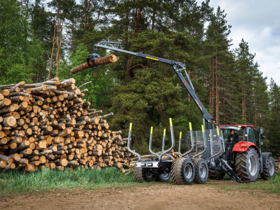Rød traktor med PALMS 10D tømmervogn som løfter en tømmerstokk foran en tømmerstabel.