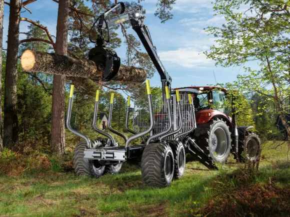 Rød traktor som laster tømmer med en robust PALMS 10D tømmervogn i skogen.