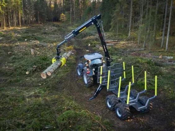 En traktor med en PALMS 7.94 skogskran løfter tømmer i et hogstfelt.