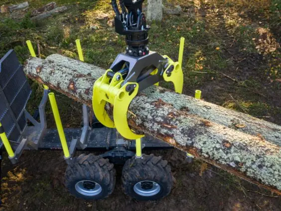 En gul og svart PALMS 7.94 skogskran løfter en stor tømmerstokk i skogen.