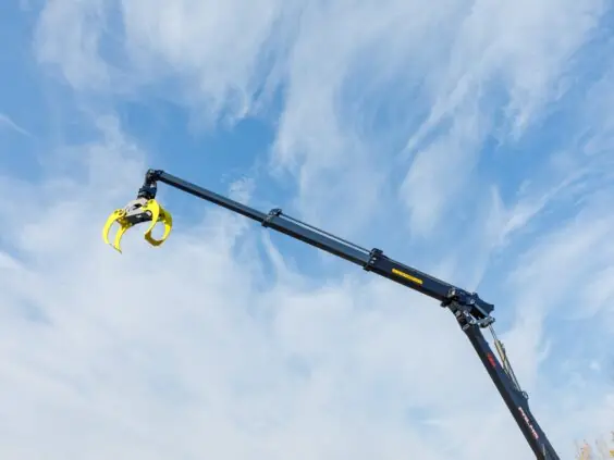 En PALMS 7.94 skogskran med gul tømmerklo hevet mot en blå og skyete himmel.