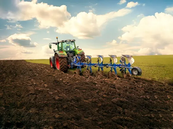 En grønn traktor utfører ploging av en åker under en skyete himmel.