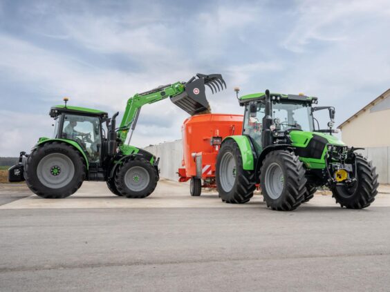 Grønn Deutz-Fahr Series 5 traktor med frontlaster fyller en oransje fôrblander på en gårdsplass.