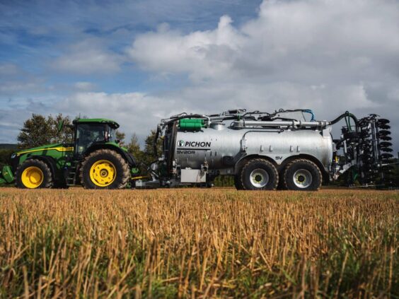 Grønn John Deere traktor med en stor Pichon gjødselvogn på en innhøstet åker.
