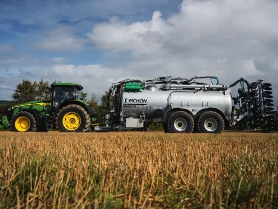Grønn John Deere traktor med en stor Pichon gjødselvogn på en innhøstet åker.