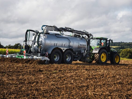 En traktor som trekker en Pichon SV-serien vakumvogn over et jorde i dagslys.