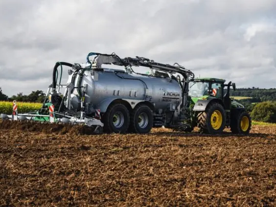 En traktor som trekker en Pichon SV-serien vakumvogn over et jorde i dagslys.
