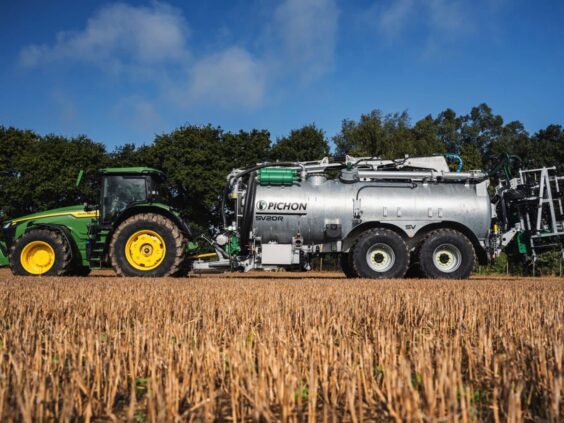Grønn traktor med en Pichon SV-serien vakumvogn på en stubbåker under blå himmel.