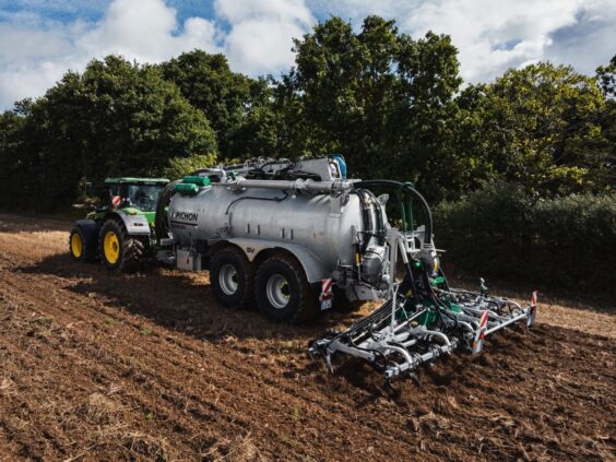 En John Deere traktor som trekker en Pichon SV-serien vakumvogn med sprederutstyr på en åker.