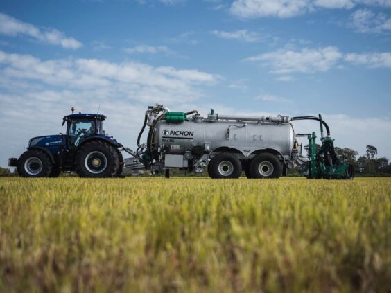 Blå traktor som trekker en Pichon SV-serien vakumvogn på en åker under blå himmel.