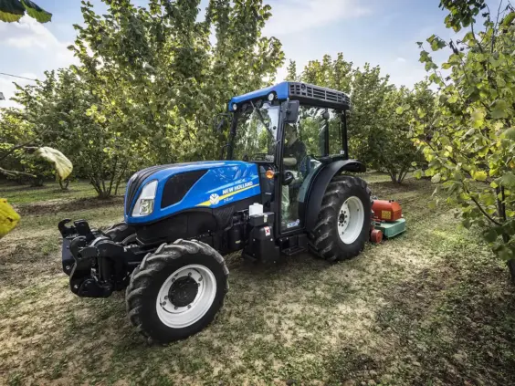 En blå New Holland T4 traktor i arbeid i en grønn frukthage.
