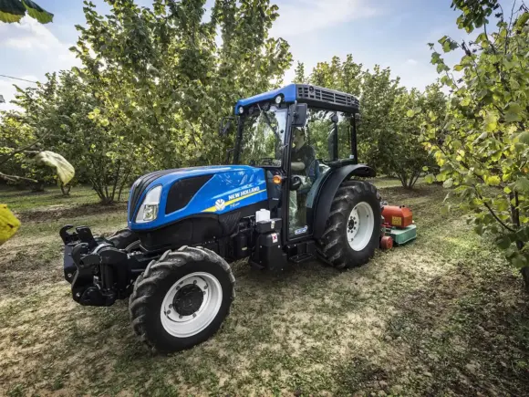 En blå New Holland T4 traktor i arbeid i en grønn frukthage.