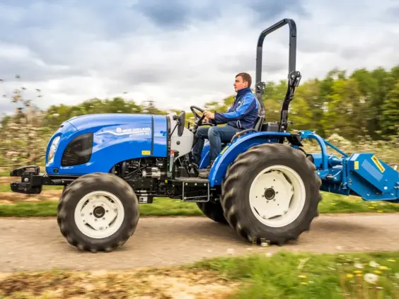 Blå mini traktor Boomer 25 C-55 i bruk på en vei i landlige omgivelser.