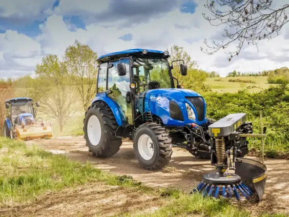 Blå Boomer 25 C-55 mini traktor med feieaggregat på en grusvei i dagslys.