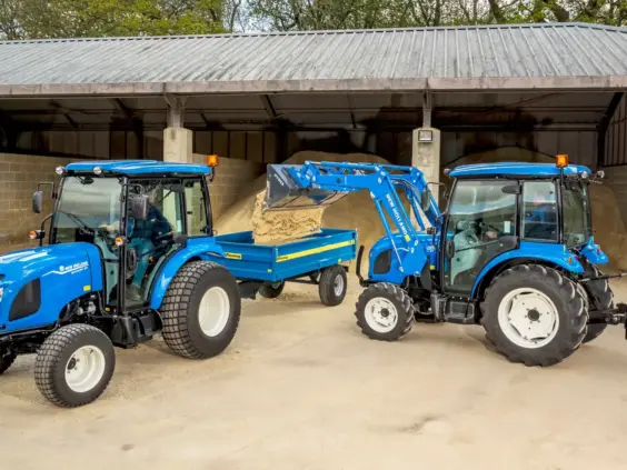 Blå mini traktor Boomer 25 C-55 laster sand i en tilhenger ved et lager.