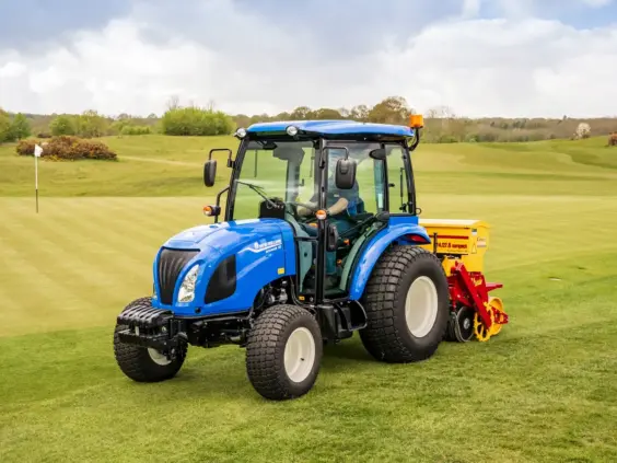En blå New Holland Boomer 25 C-55 mini traktor i arbeid på en golfbane.