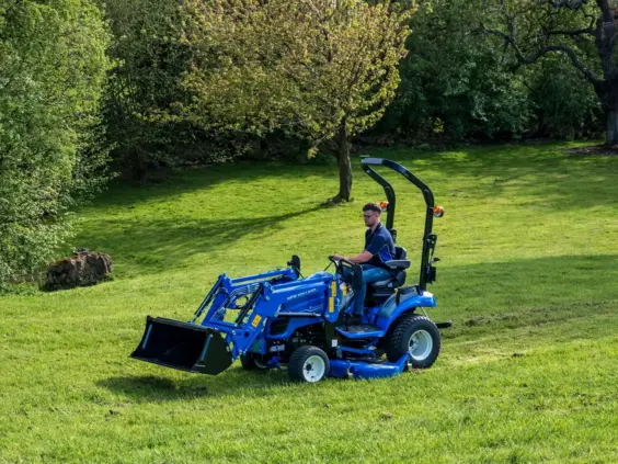 En blå Boomer 25 C-55 mini traktor med frontlaster på en grønn gressplen.