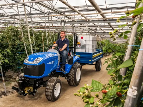 Blå Boomer 25 C-55 mini traktor som trekker en vanntank gjennom et grønt drivhus.