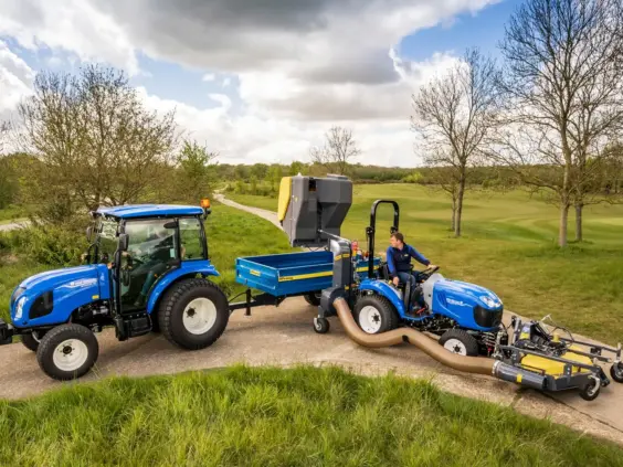 Blå mini traktor Boomer 25 C-55 i arbeid med gressklipping på en parkvei.